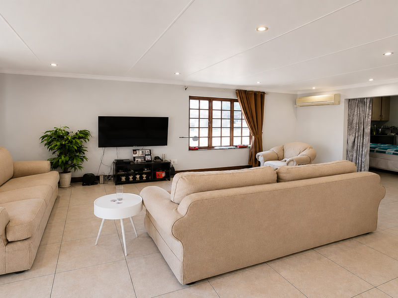 Spacious living room featuring neutral tiled flooring, recessed downlighting, and a wall-mounted air conditioning unit, with an open transition to an adjacent room.