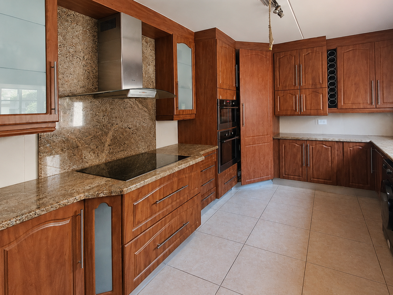 A spacious kitchen featuring warm-toned wooden cabinetry, granite countertops, integrated appliances, and neutral ceramic floor tiles.