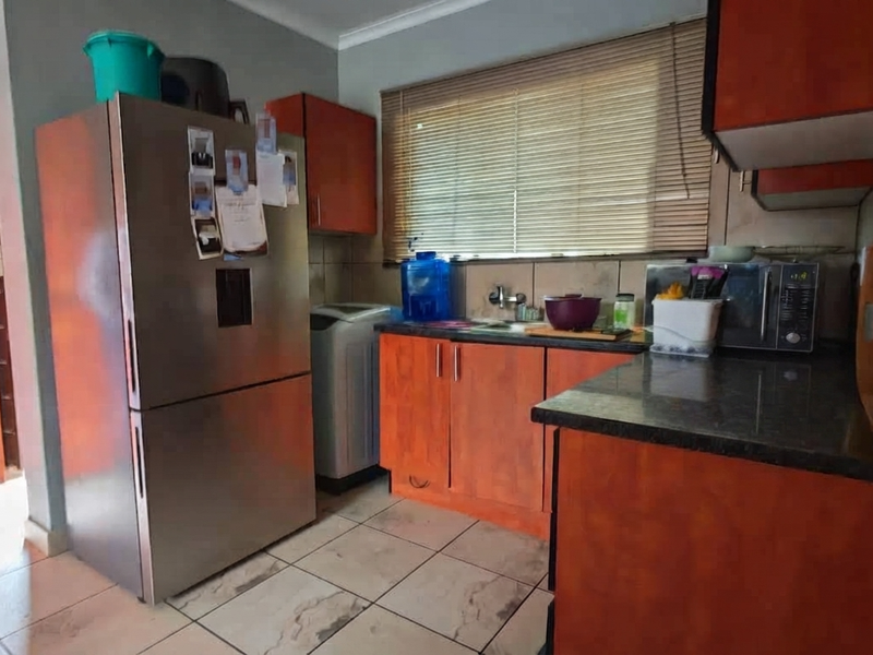 A functional kitchen featuring wood-finish cabinetry, dark countertops, tiled flooring, and a window with venetian blinds, providing a practical workspace.