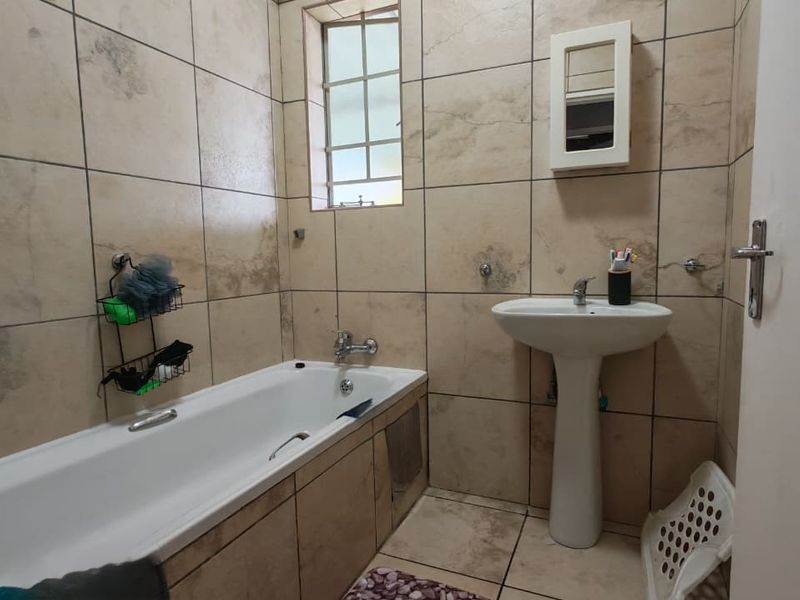 A functional bathroom featuring a pedestal basin, a built-in bathtub, and neutral wall and floor tiling.