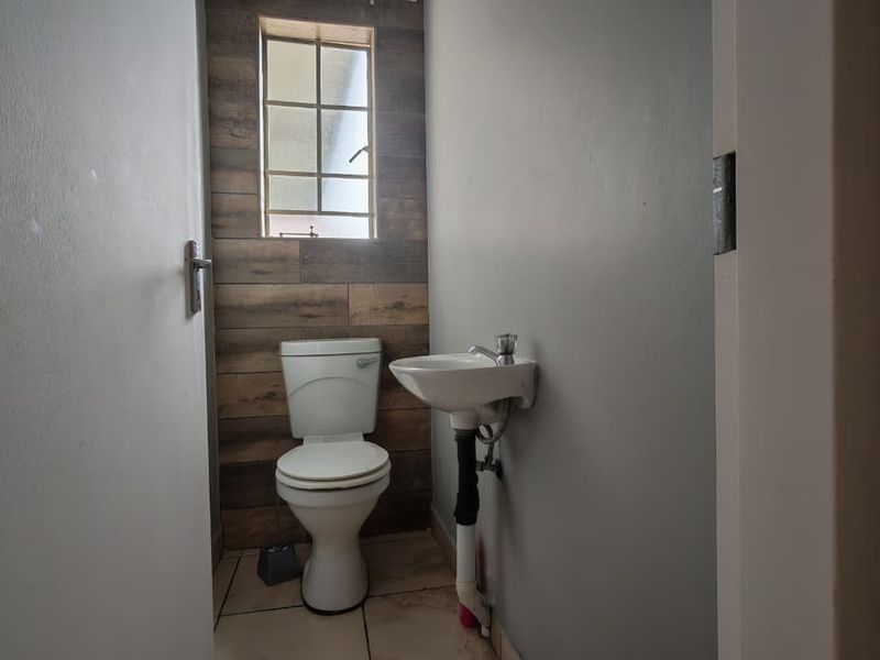 A compact guest bathroom featuring a toilet, wall-mounted basin, and a decorative tiled feature wall.