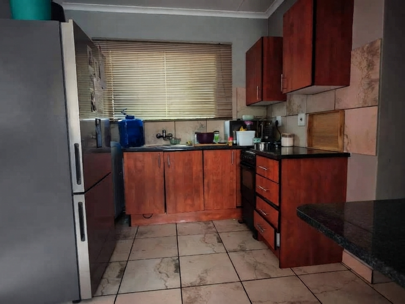 A functional kitchen featuring wooden cabinetry, granite countertops, tiled backsplash, and tiled flooring, offering a practical layout for daily meal preparation.