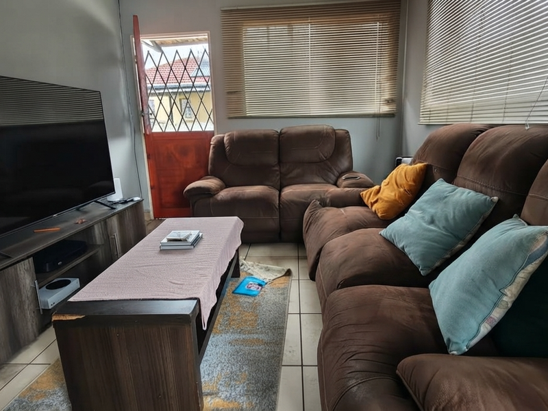 A functional living room featuring tiled flooring, venetian blinds, and a security gate leading to the exterior.