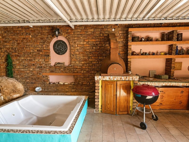Covered outdoor entertainment area featuring a built-in jacuzzi, brick pizza oven, and integrated shelving, providing a rustic space for relaxation and dining.