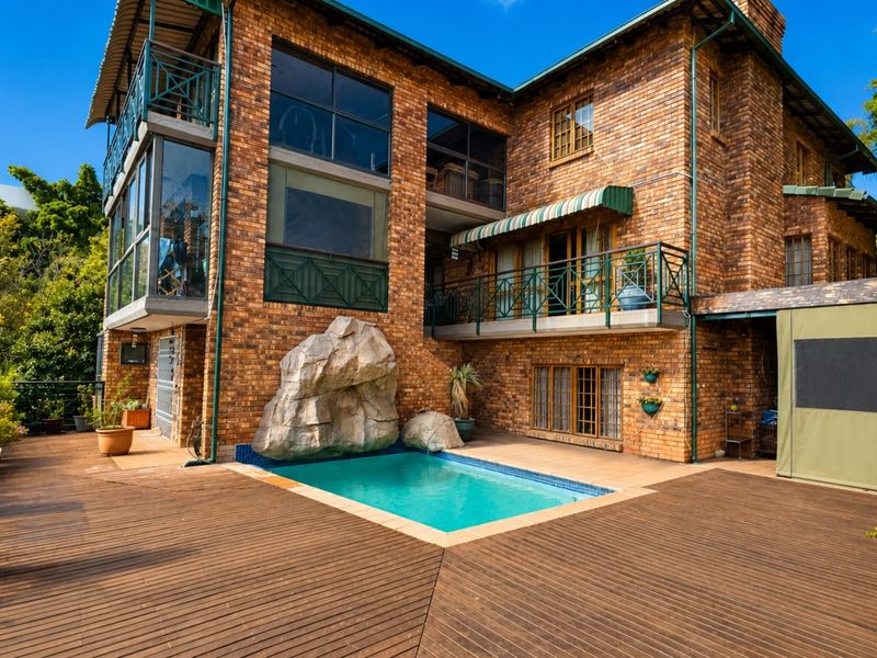 Rear exterior view featuring a multi-story brick house with a swimming pool, timber decking, and a balcony with metal railings.