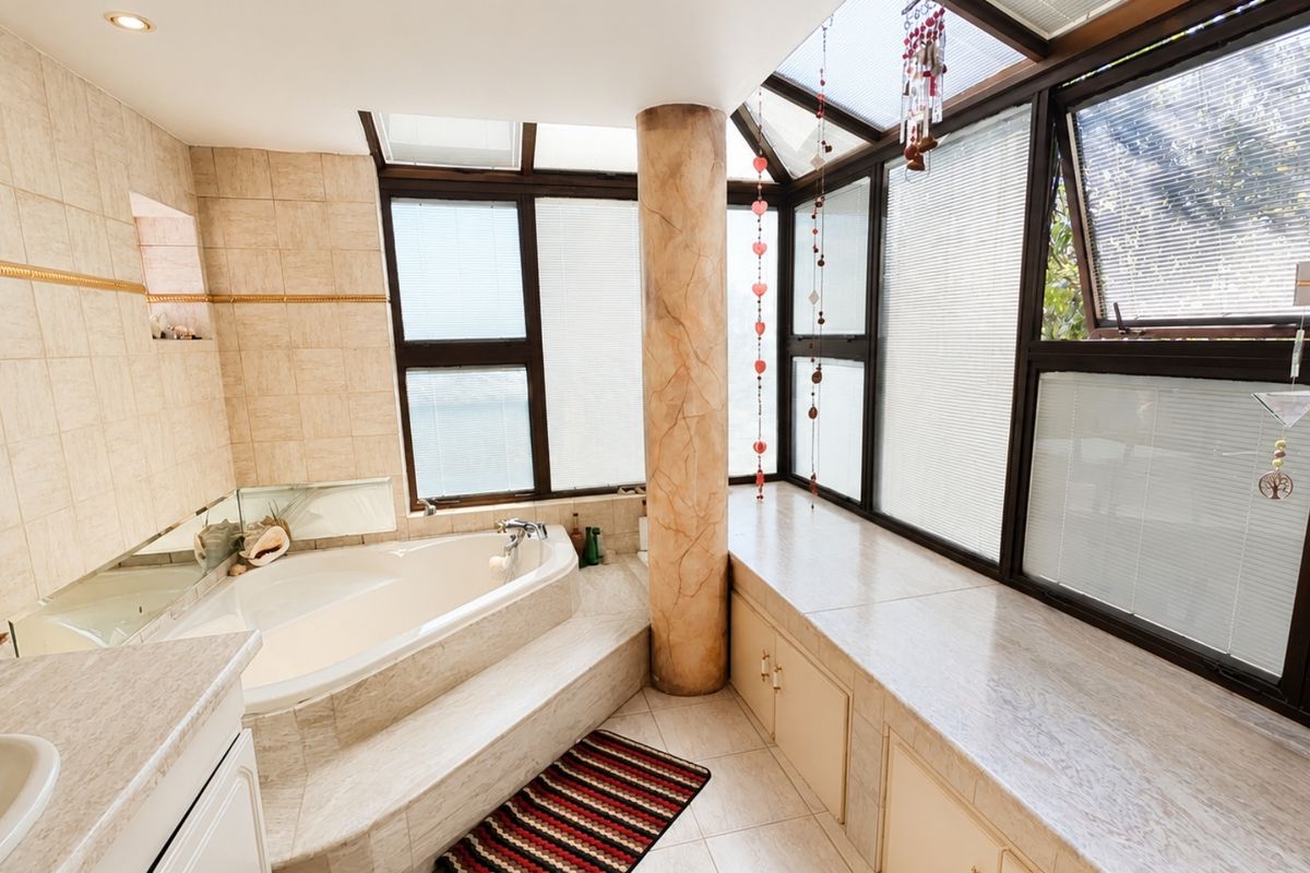 Spacious bathroom featuring a built-in corner bathtub, extensive stone-topped vanity cabinetry, and a large skylight providing ample natural light.