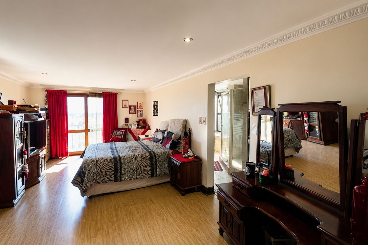 Spacious bedroom featuring laminate flooring, crown molding, recessed lighting, and an attached en-suite bathroom with direct access to a balcony through sliding glass doors.
