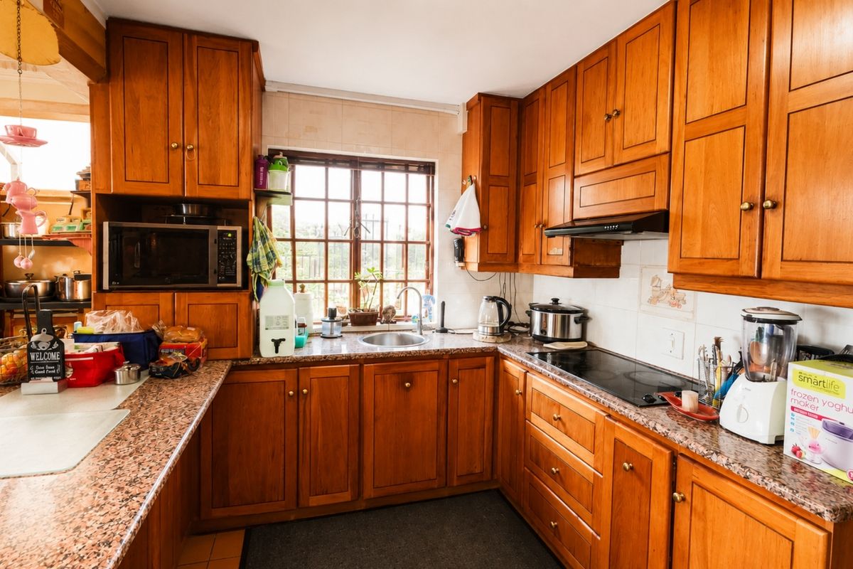 A functional kitchen featuring warm wooden cabinetry, granite countertops, a built-in hob with extractor fan, and a classic lattice window.