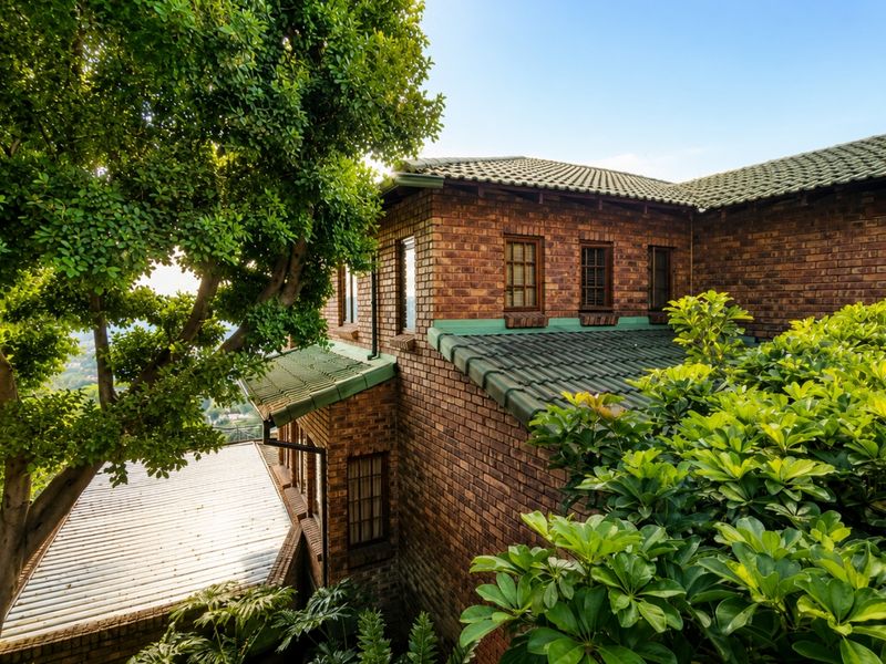 A view of the rear elevation featuring classic face brick construction, green tiled roofing, and established surrounding greenery.