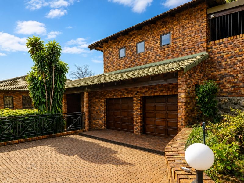 A well-maintained face brick house exterior featuring a double garage, paved driveway, and landscaped garden elements.