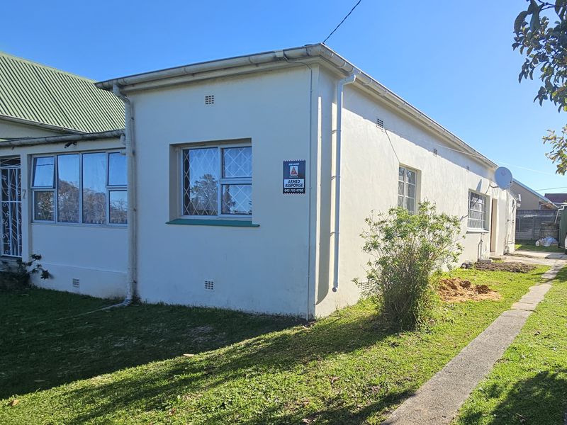 Rear exterior view of the townhouse featuring white painted walls, aluminium window frames with security bars, and a concrete pathway leading along the side.