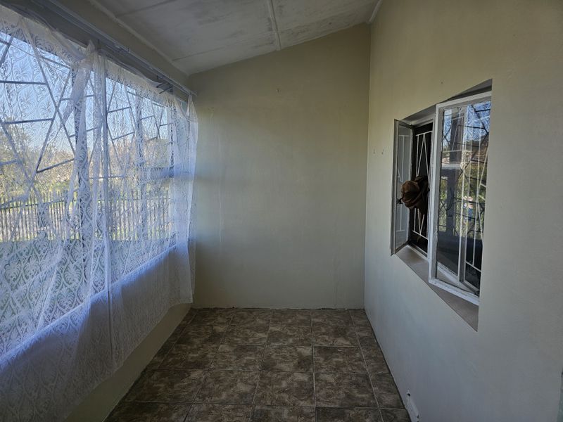 An enclosed patio or sunroom featuring tiled flooring and security bars on the windows, offering a versatile space for potential renovation.