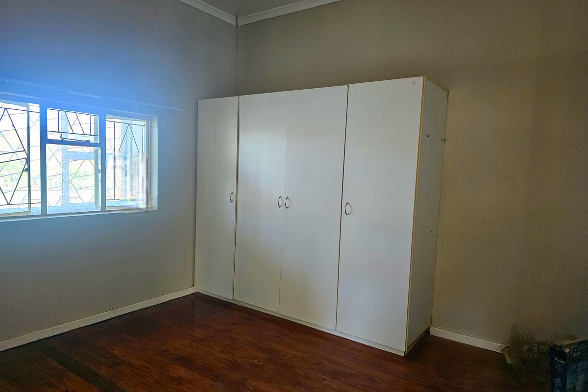 A bedroom featuring polished wooden flooring, a built-in white wardrobe, and a window fitted with security bars.