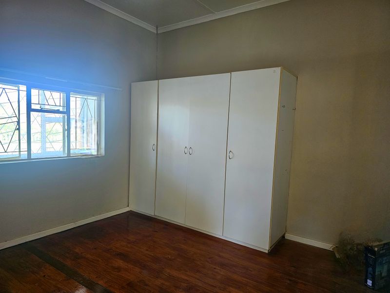A bedroom featuring polished wooden flooring, a built-in white wardrobe, and a window fitted with security bars.