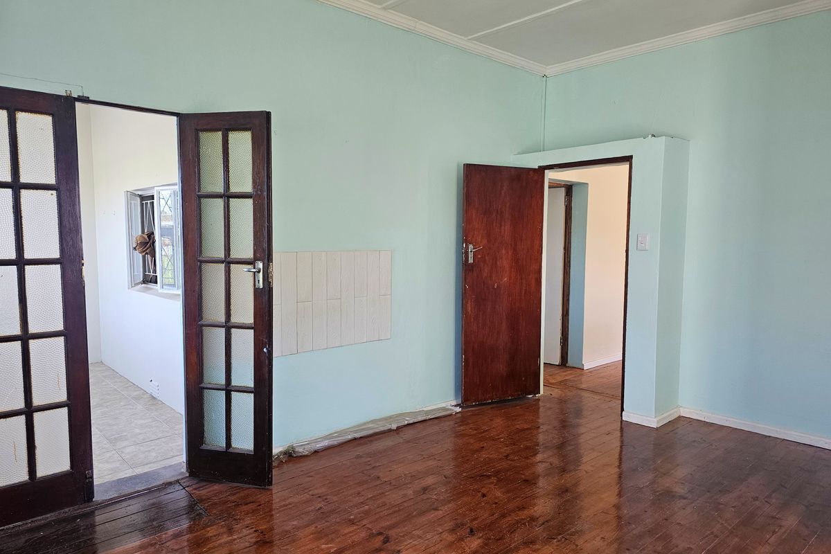 An empty living room featuring polished timber flooring, classic french doors, and neutral wall paint, offering a blank canvas for interior design.
