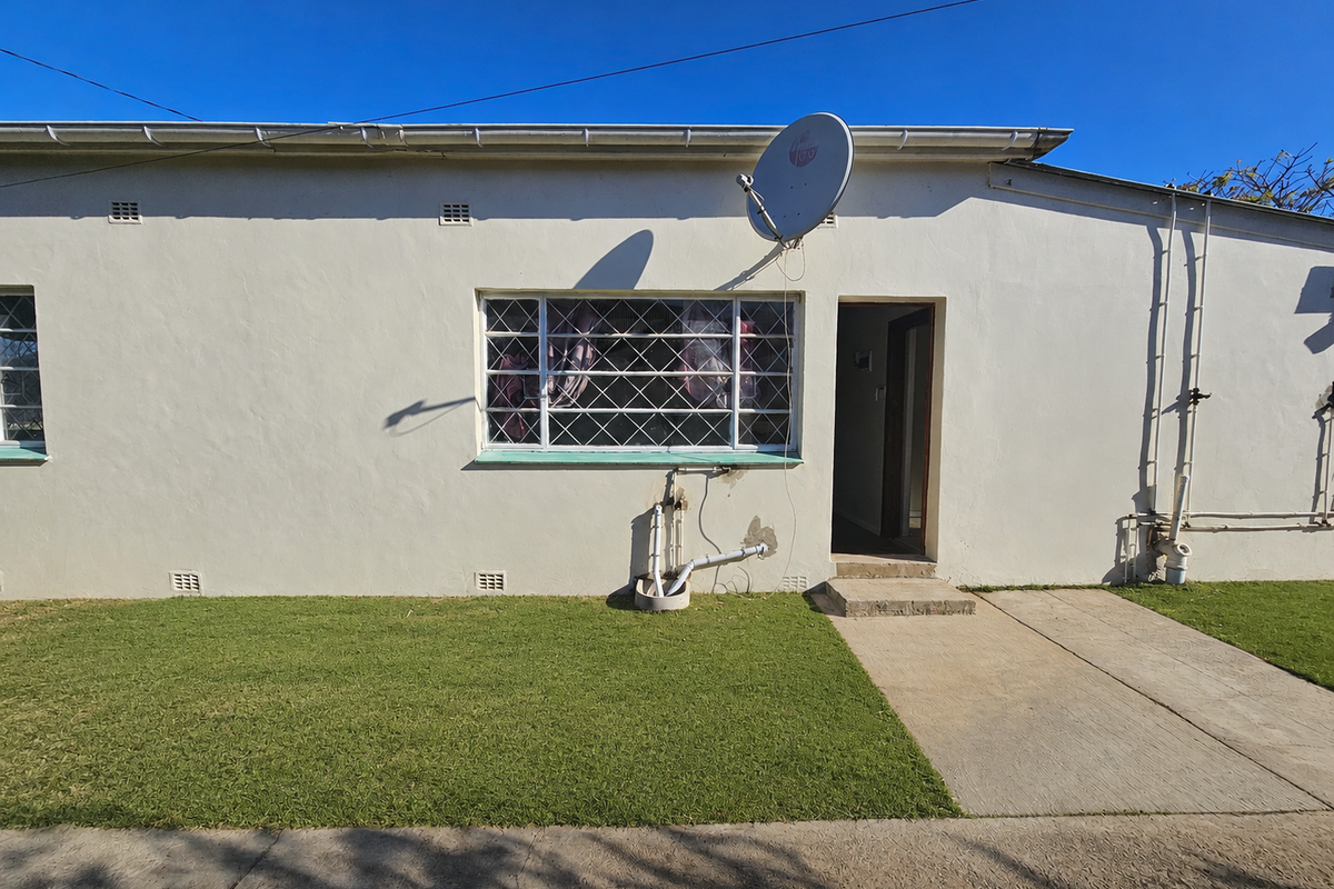 Rear exterior view of the townhouse featuring a concrete walkway, lawn area, and wall-mounted satellite dish.