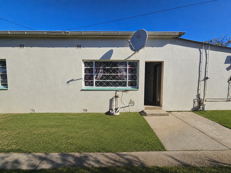 Rear exterior view of the townhouse featuring a concrete walkway, lawn area, and wall-mounted satellite dish.