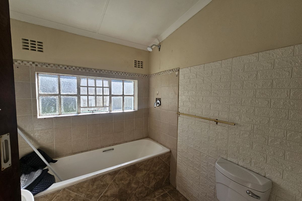 A dated bathroom featuring a built-in bathtub, shower head, and toilet, with tiled wall accents and a window for natural light.