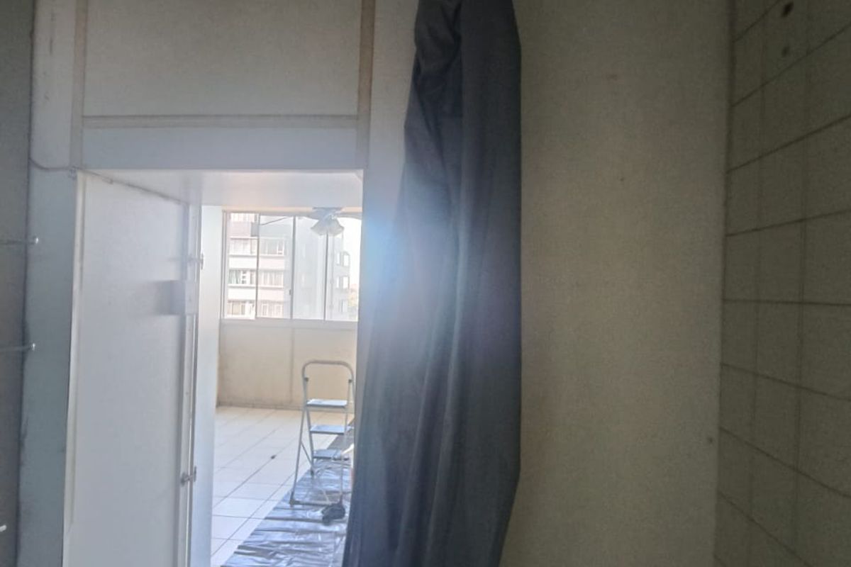 A bathroom interior in need of renovation, featuring tiled surfaces and an unfinished ceiling, with a view through to an adjacent balcony area.