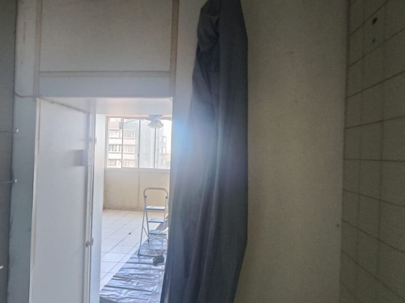 A bathroom interior in need of renovation, featuring tiled surfaces and an unfinished ceiling, with a view through to an adjacent balcony area.