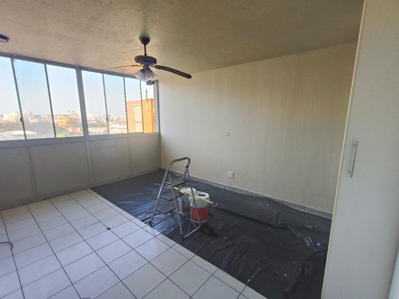 An enclosed balcony area featuring tiled flooring, a ceiling fan, and a built-in cupboard, currently undergoing minor maintenance and painting.