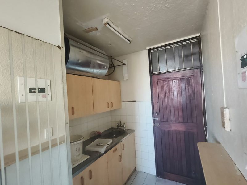 A functional scullery or utility area featuring built-in cabinetry, a sink, and an exposed geyser, requiring cosmetic updates to improve its condition.