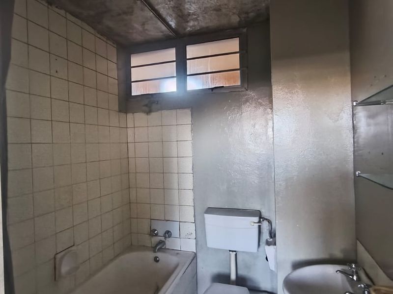 A dated bathroom featuring a bathtub, pedestal basin, and toilet, requiring significant renovation and cosmetic updates to improve its condition and functionality.