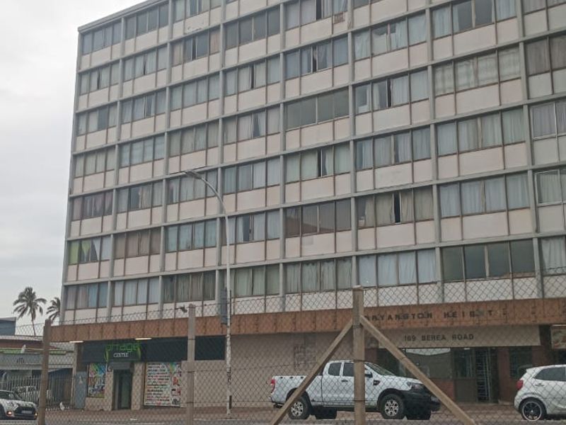 Street-level view of a multi-story apartment building featuring a large facade with numerous windows and ground-floor commercial units.