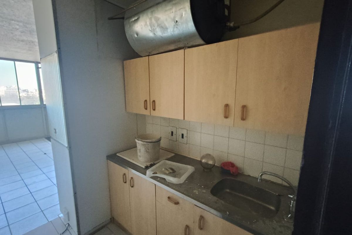 A compact scullery area featuring built-in cabinetry, a stainless steel sink, and a wall-mounted electric water heater, requiring significant refurbishment.