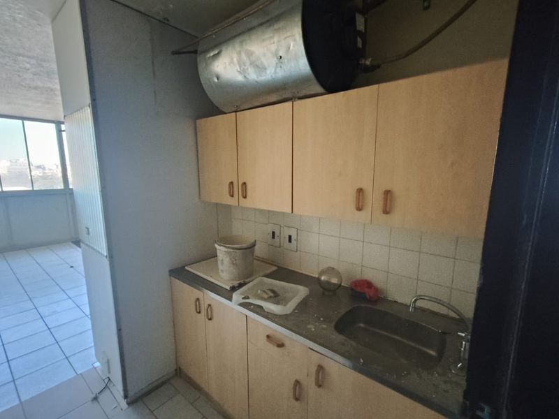 A compact scullery area featuring built-in cabinetry, a stainless steel sink, and a wall-mounted electric water heater, requiring significant refurbishment.