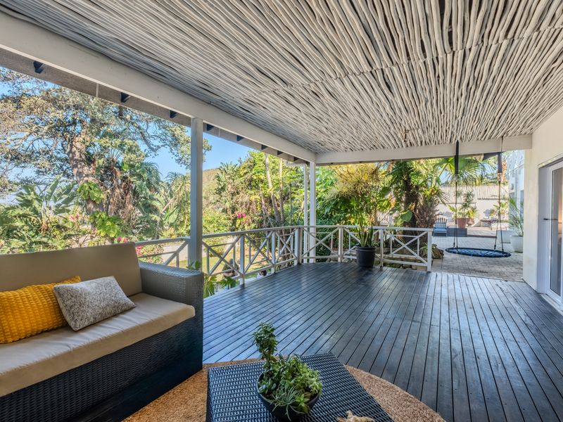 Spacious covered patio featuring timber decking, a rustic thatched ceiling, and a timber balustrade overlooking the garden.