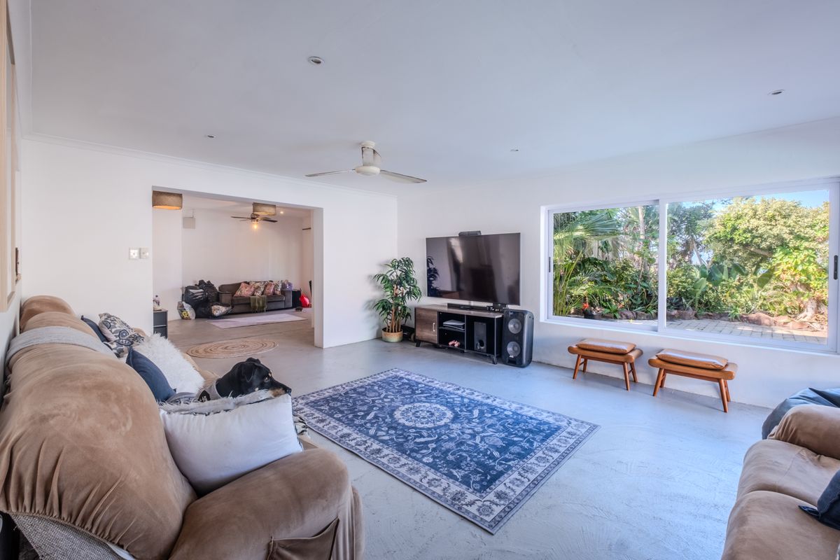 Spacious living room featuring concrete flooring, recessed lighting, a ceiling fan, and large sliding glass doors providing natural light and garden views.