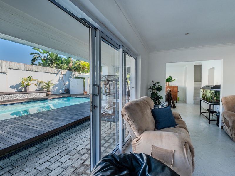 Open plan living area featuring large sliding glass doors that open onto a timber deck and swimming pool area.