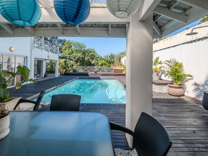 Outdoor entertainment area featuring a swimming pool, timber decking, and a covered patio space with an integrated outdoor shower.