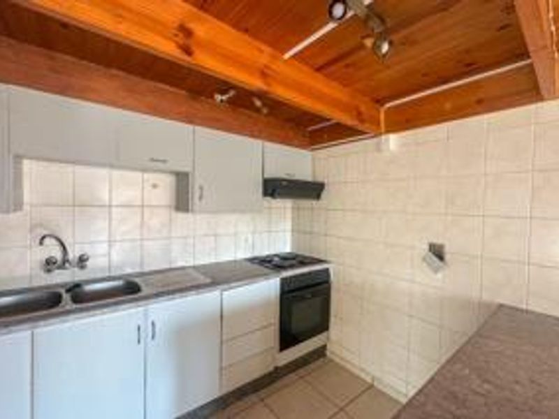 A functional kitchen featuring built-in cabinetry, a double sink, integrated oven and hob, and a distinctive exposed timber beam ceiling.