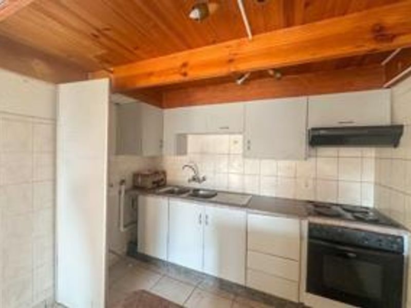 A compact kitchen featuring built-in cabinetry, a stainless steel sink, an integrated oven and hob, and exposed timber ceiling beams.