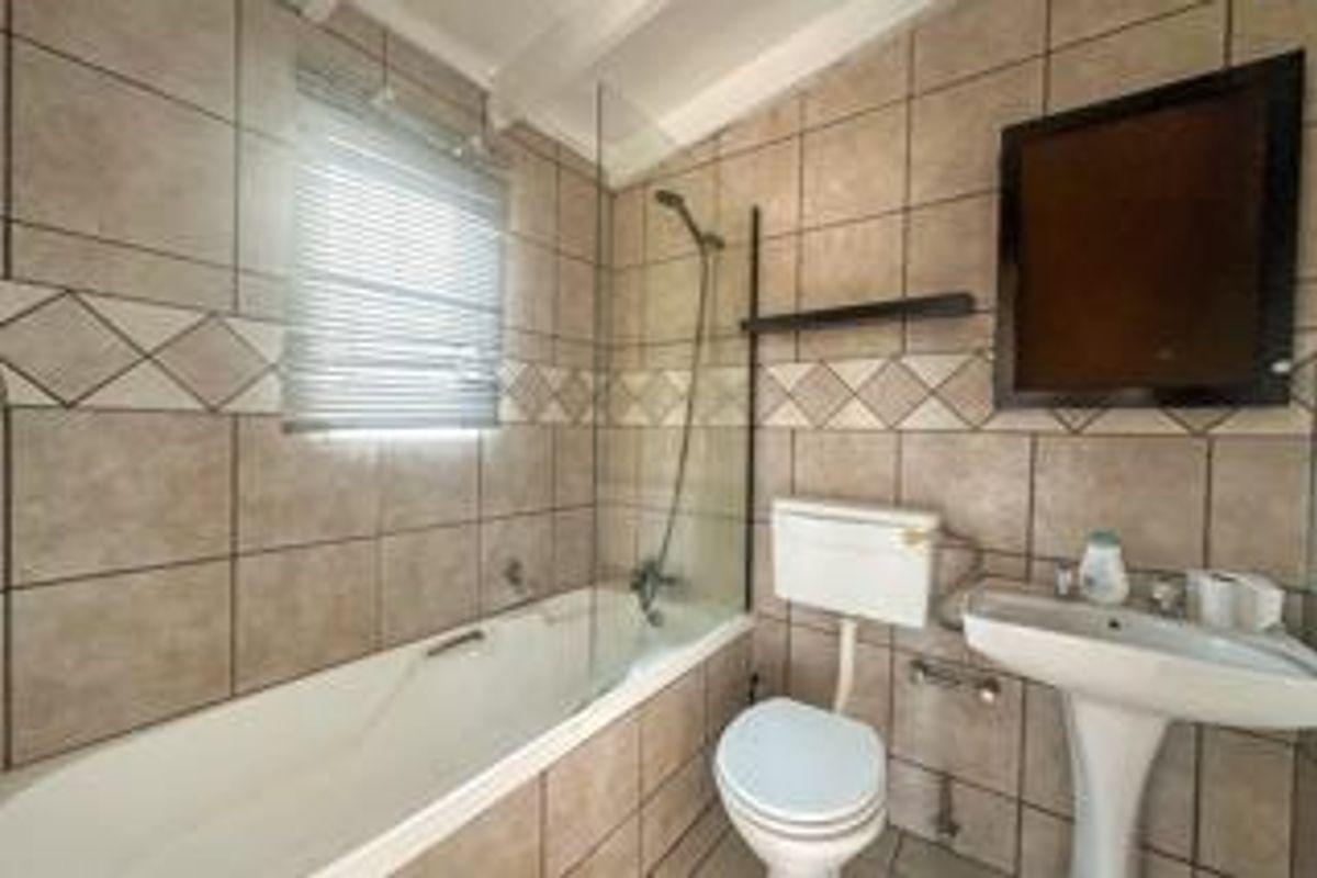 A functional bathroom featuring a bathtub with a glass screen, pedestal basin, and toilet, finished with neutral wall tiling.