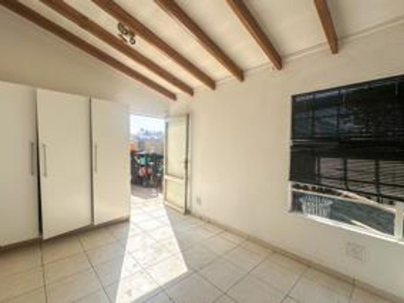 A bright, empty bedroom featuring tiled flooring, exposed timber ceiling beams, and built-in cupboards, with direct access to an outdoor area.