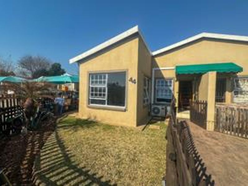 Front exterior view of the flat featuring a paved walkway, timber fencing, and a small garden area with an installed air conditioning unit.