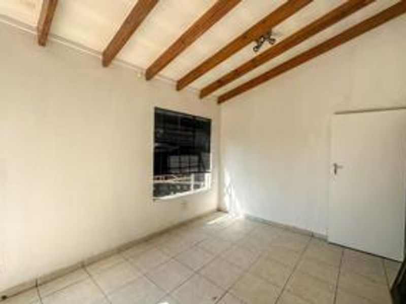 An empty bedroom featuring exposed timber ceiling beams, tiled flooring, and a window with security bars.