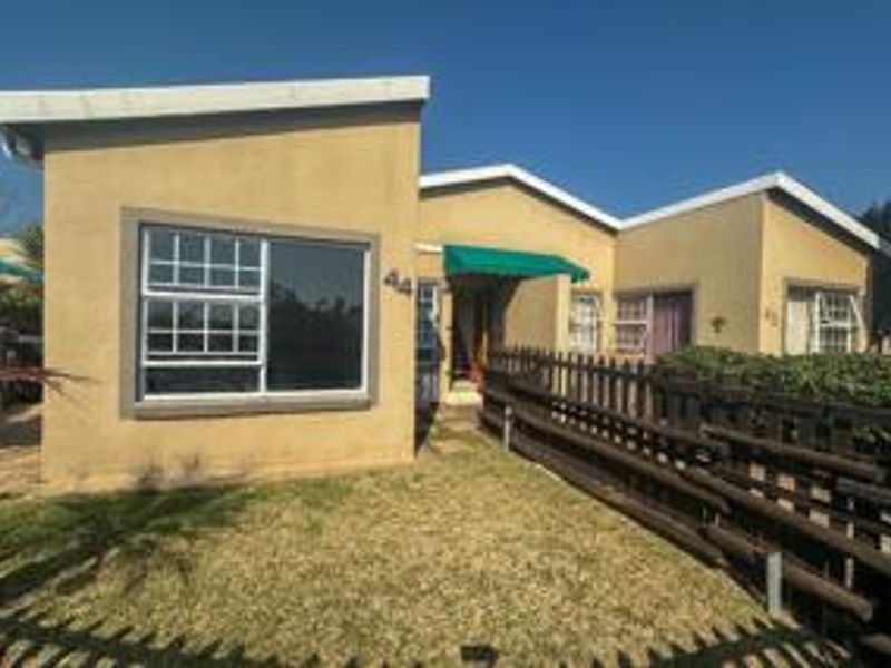 Front elevation of a single-story flat featuring stucco walls, timber fencing, and a green entrance awning.