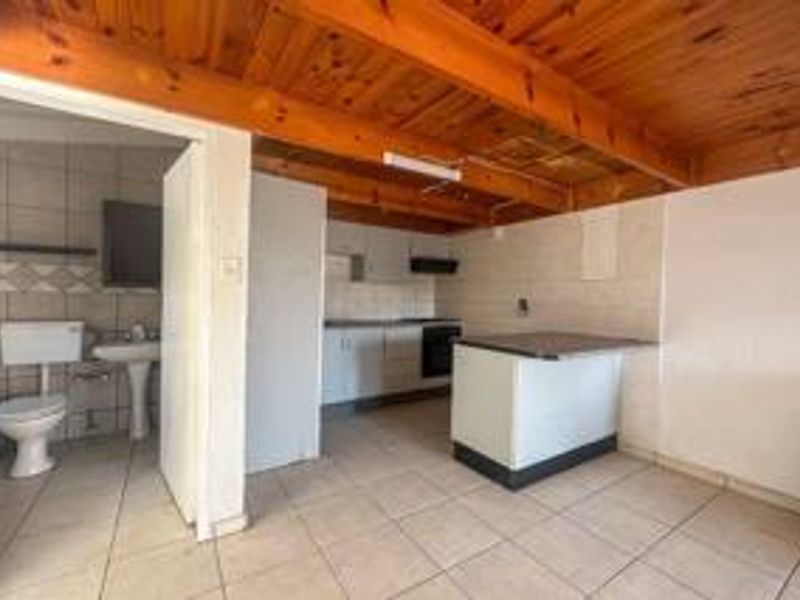 Open plan kitchen and living area featuring exposed timber beams, tiled flooring, and an adjacent bathroom with standard fixtures.