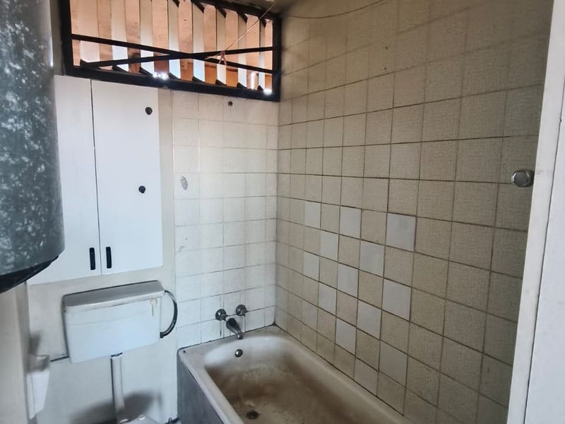 A dated bathroom featuring a bathtub, toilet, and wall-mounted cabinet, requiring significant renovation and modernization of all fixed finishes and fixtures.