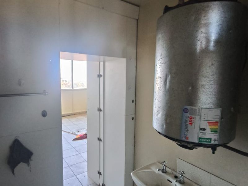 A utility space featuring a wall-mounted electric water heater, a small basin, and tiled flooring, currently in need of maintenance and cosmetic updates.