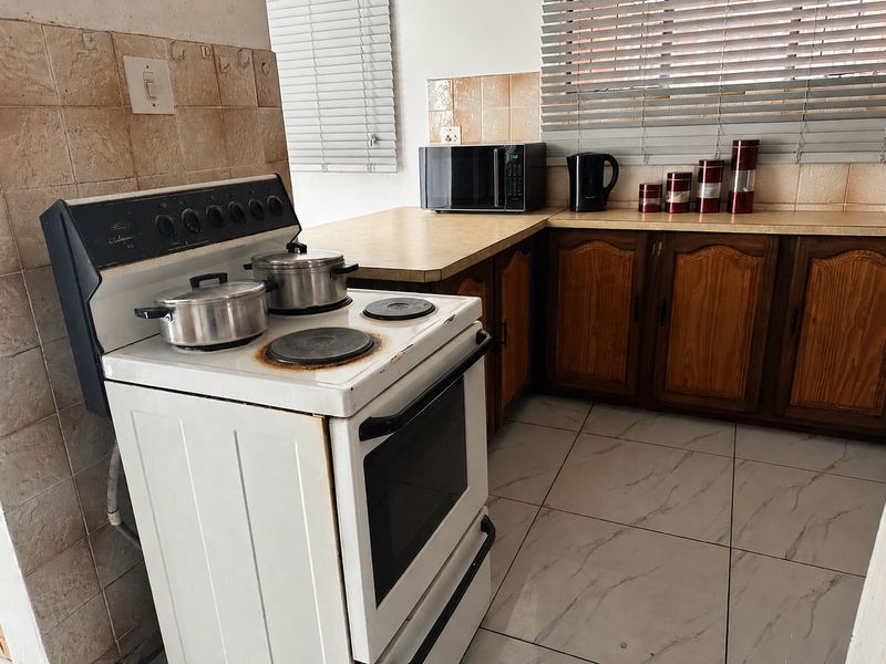 A dated kitchen featuring wooden cabinetry, laminate countertops, tiled backsplash, and a freestanding stove, offering potential for a modern renovation.