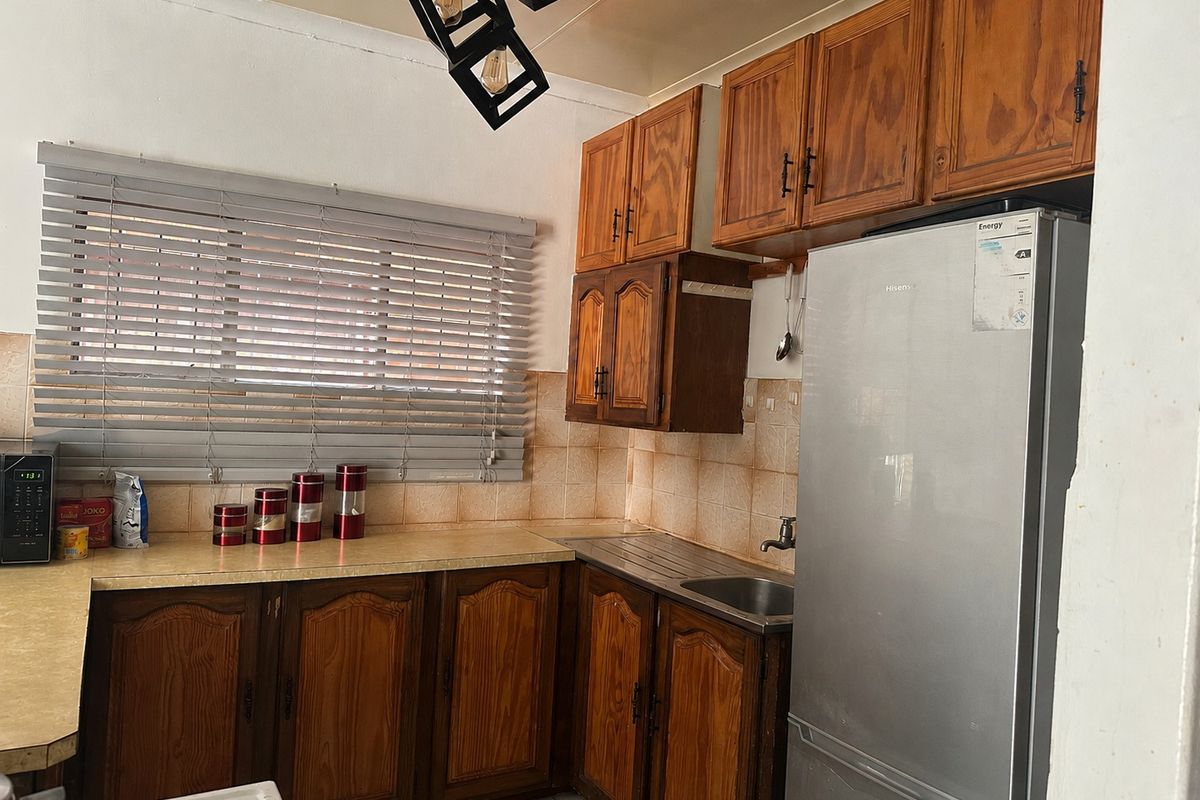 A functional kitchen featuring traditional wooden cabinetry, laminate countertops, a stainless steel sink, and a tiled backsplash with natural light from a window.