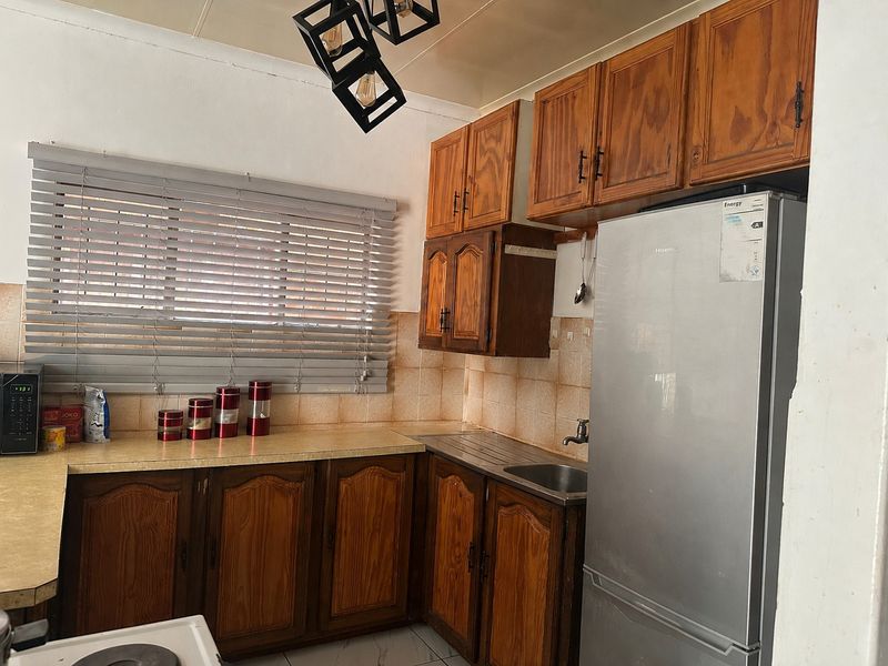 A functional kitchen featuring traditional wooden cabinetry, laminate countertops, a stainless steel sink, and a tiled backsplash with natural light from a window.