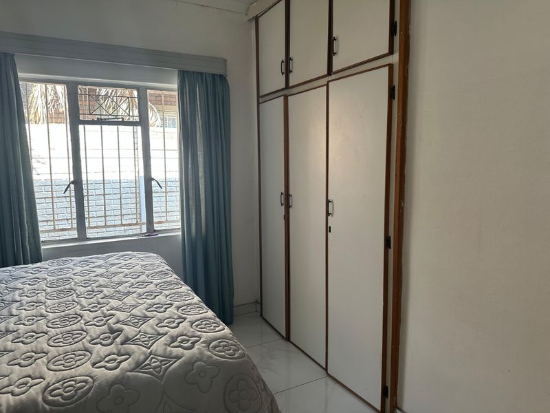 Bedroom featuring built-in cupboards, tiled flooring, and a window with security bars, offering a functional space with potential for cosmetic updates.