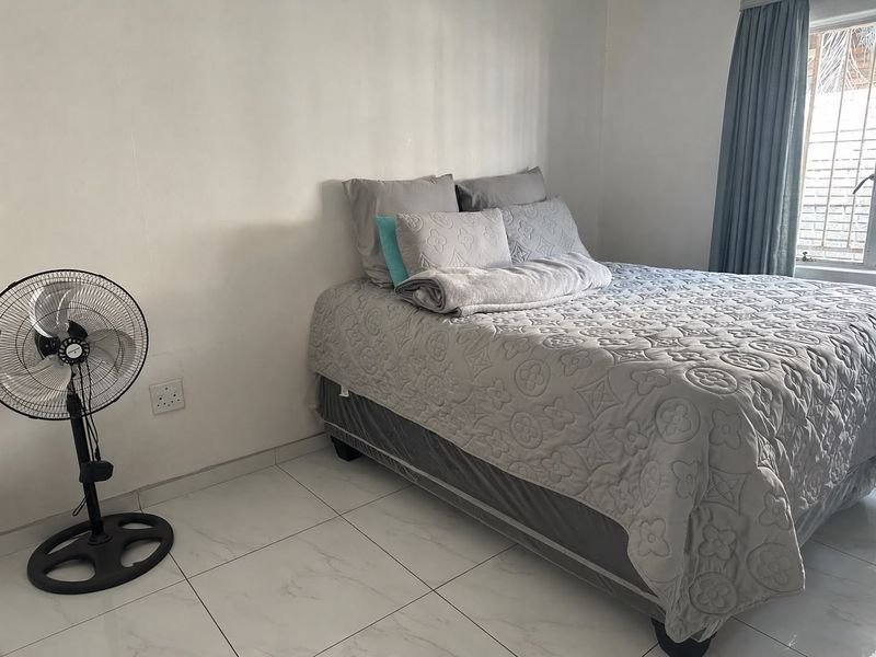 A simple bedroom featuring white tiled flooring and a window fitted with security bars.