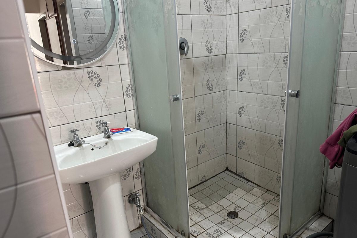 A functional bathroom featuring a pedestal washbasin, a glass-enclosed shower, and patterned wall tiling.